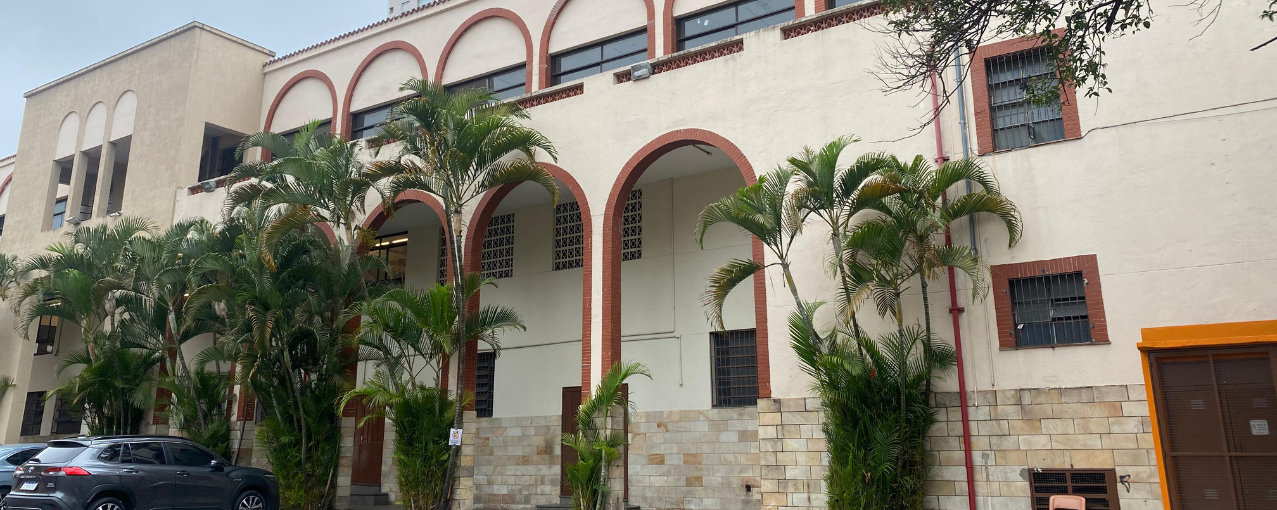 Na imagem, consta a entrada da Missão Paz. Com algumas árvores dispostas entre os arcos da fachada da instituição.